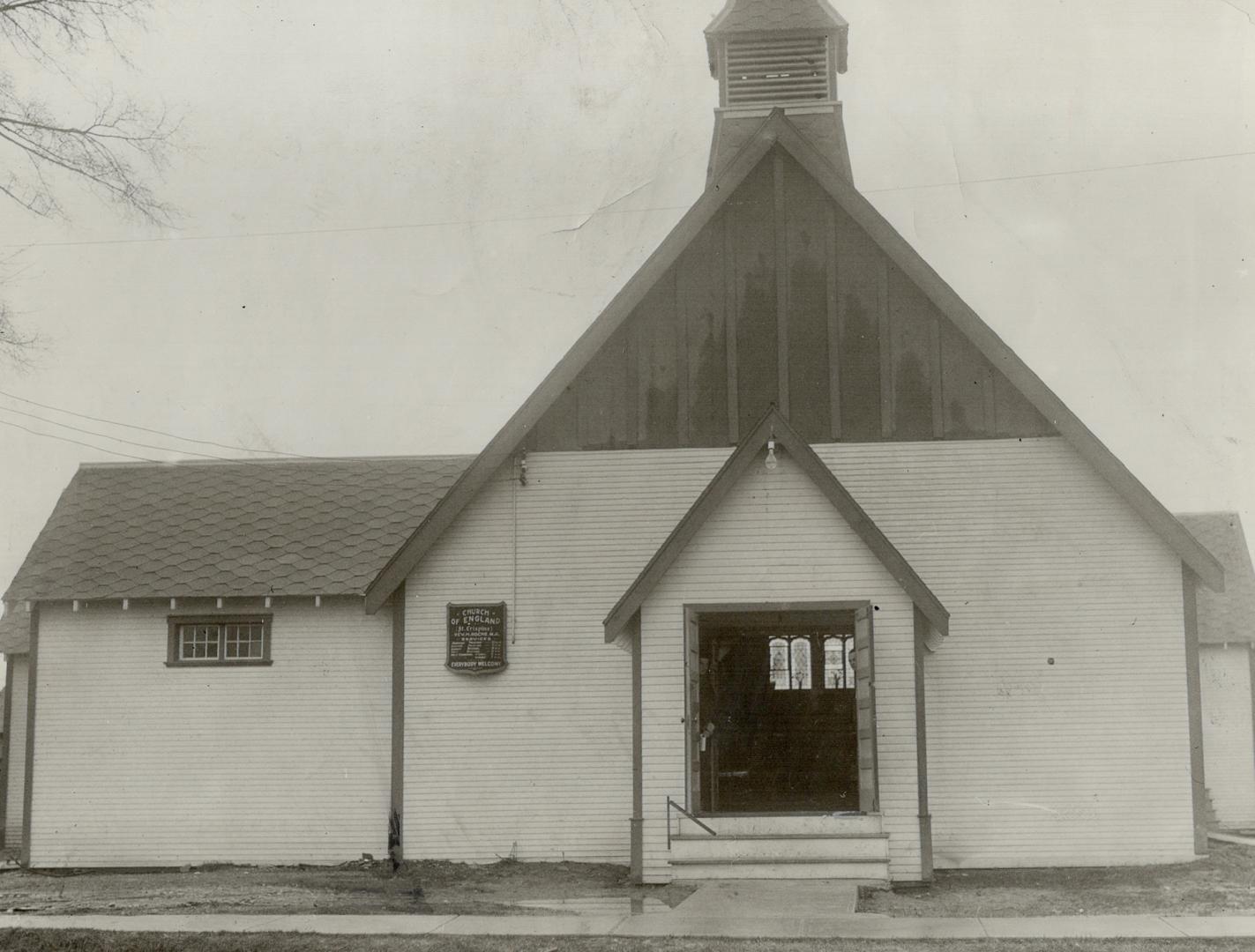 Exterior of church with white siding, honeycomb tile on left roof and small belfry tower above …