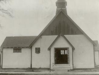 Exterior of church with white siding, honeycomb tile on left roof and small belfry tower above …