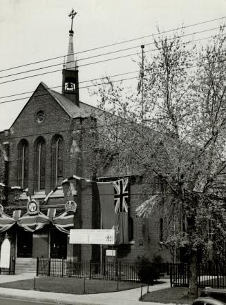 Exterior of brick church with Union Jack flags draped above entrance and replica crown affixed,…