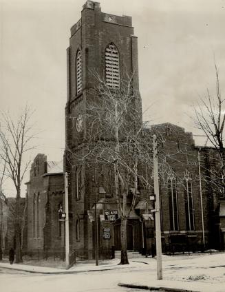 Exterior of brick church with elongated arched windows and prominent belfry tower. Sign hanging…