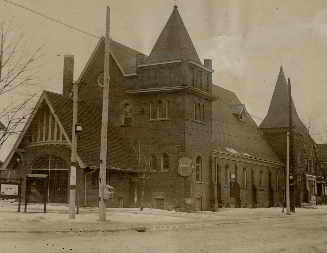 Exterior of brick church with steep gable roof and attached towers front and rear. Front gabled…