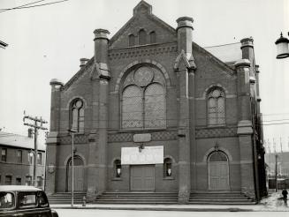 Front exterior of brick church with arched windows and entrance doors.