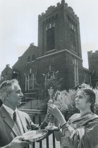 In foreground, a man and woman look towards a flame rising from a candle holder held jointly be…