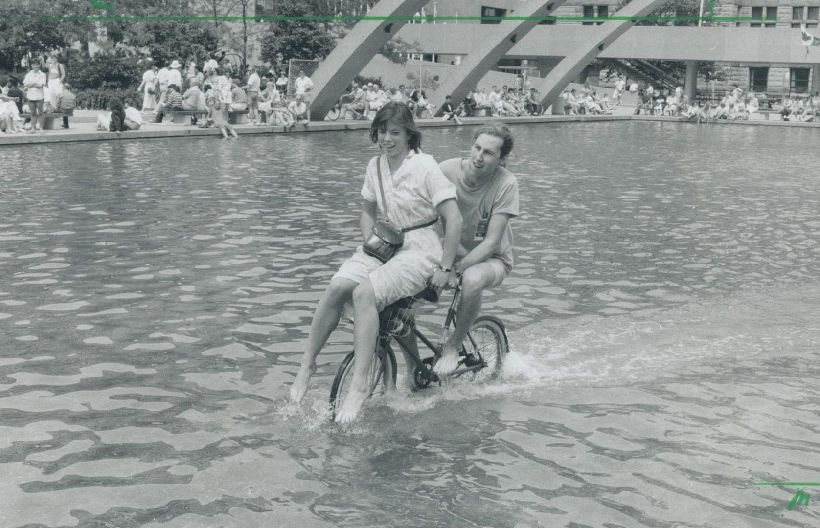 Making a splash on two wheels, Gem Blanston takes Laurie Deviney for a cooling spin in his bike basket carrier around the reflecting pool at Nathan Phillips Square