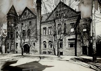 Façade of three-storey brick and stone building featuring a turret and two gabled roof sections…