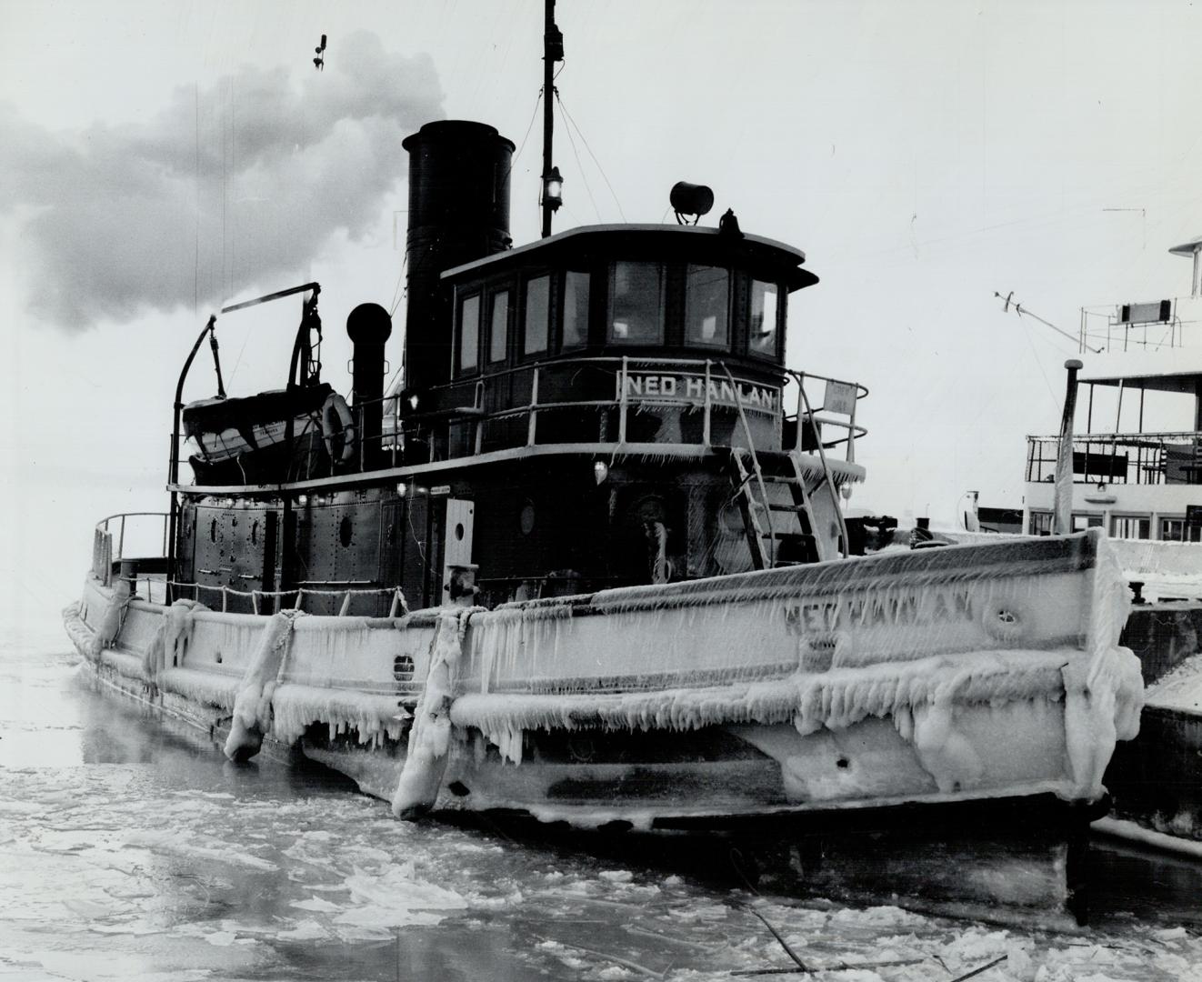 Festooned with ice, The Ned Hanlan ties up in Toronto, Wind-whipped spray freezes on the tug as it moves about the harbor