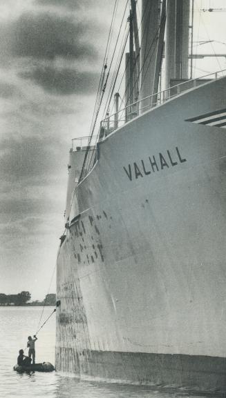 Image shows two people on a small boat besides a huge cargo ship.