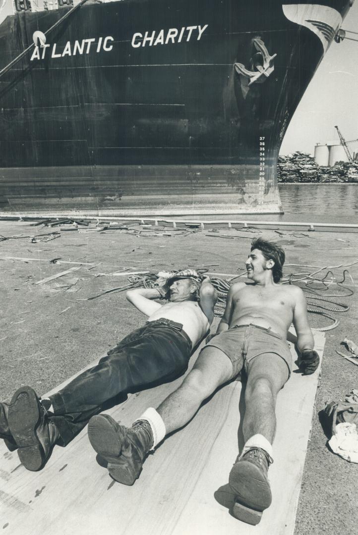 Image shows two workers resting at the Harbour with the ship "Atlantic Charity" in the backgrou…