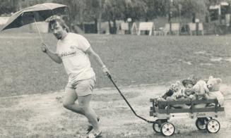 Bearing up to the rain. Pete Barham carries umbrella as he pulls wagon loaded with nephews Tim Groves, 5, left, and Jeff, 2, and assorted teddy bears (...)