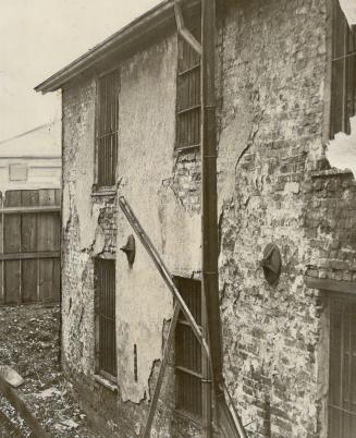 This photograph, snapped through a crack in the fence, shows the dilapidated condition into which the historic old buildings of Fort York have fallen