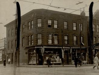 Three-storey brick building at corner of intersection. Shop window at street level displays clu…