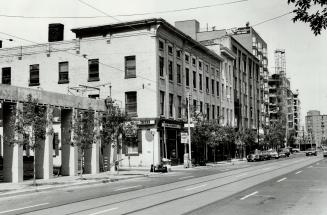 Streetscape showing three-storey brick building in the foreground with a sign above the ground …