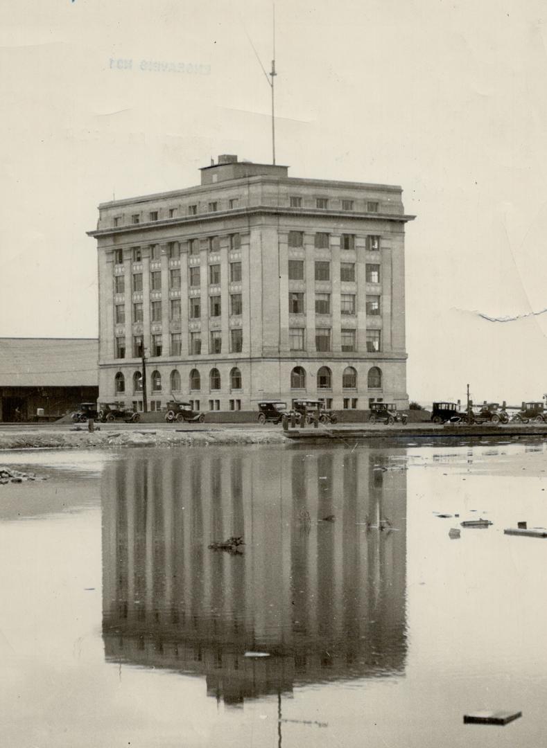 Façade of six-storey building with image reflected by water in foreground.