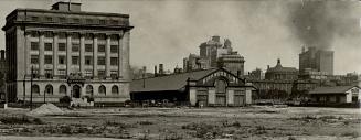 A six-storey building overlooking a patch of barren land stands left of a factory with a sign r…