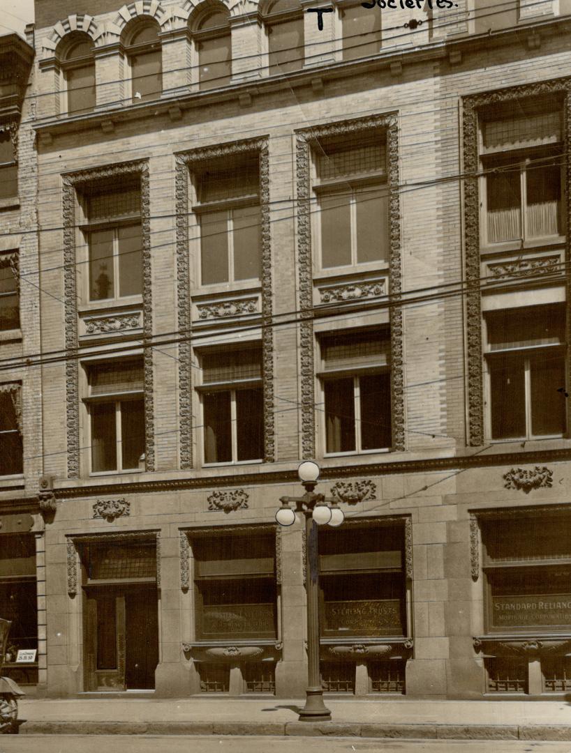 Façade of four-storey brick building with decorative stonework framing windows. Signs in the gr…