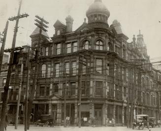 Four-storey brick building with turret at corner of intersection. Sign above entrance reads, C.…