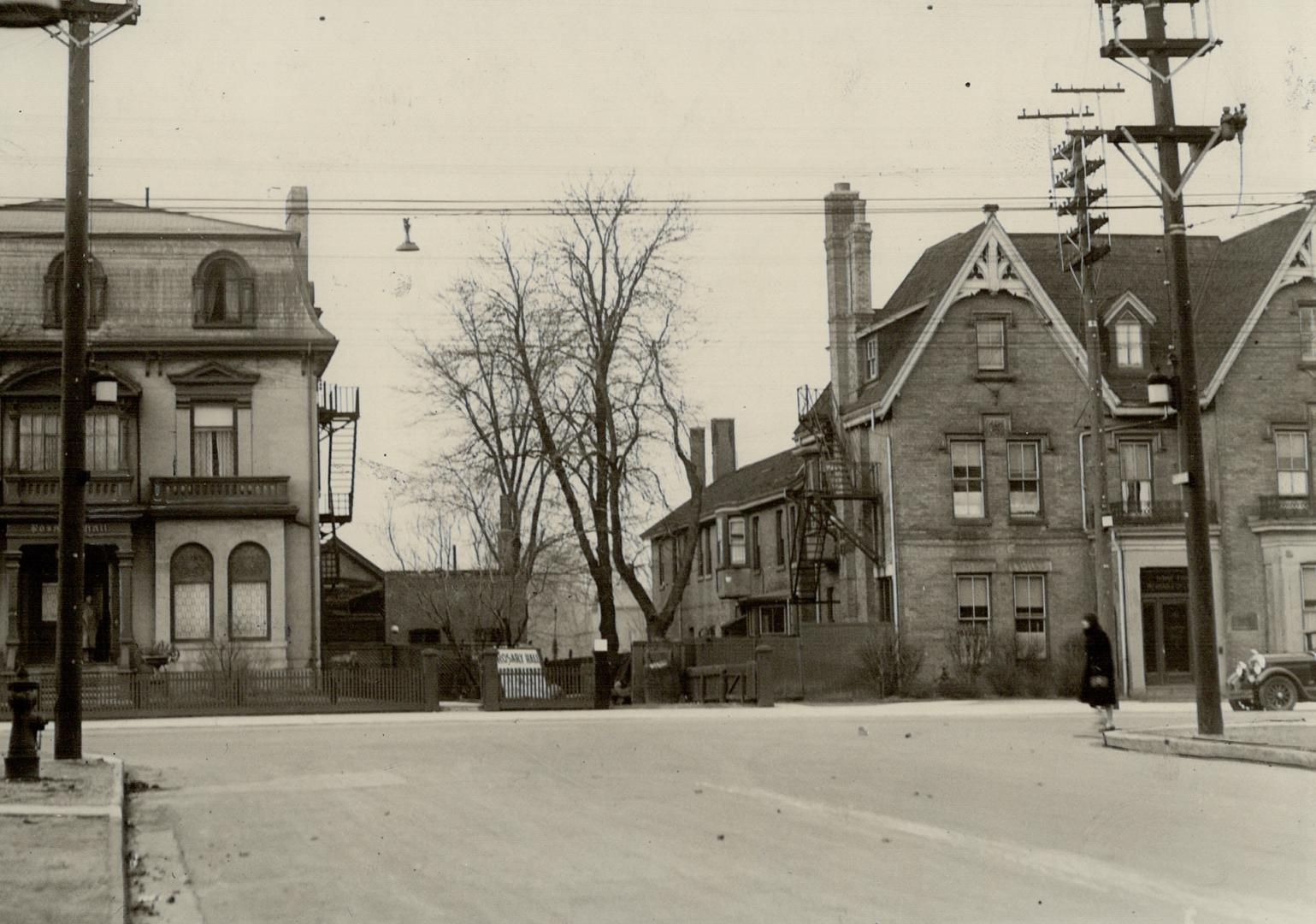 Street view showing two three-storey brick houses at intersection; house on left has Mansard ro…