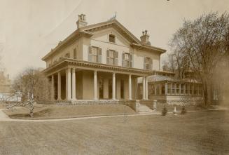  Two-storey structure with sloped roof, two visible brick chimneys, wraparound porch and attach…