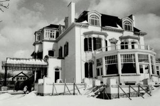  Three-story light brick house with dark roof, covered entrance, and protruding solarium. Wood …