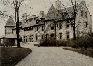 Three-storey, chiseled stone structure with shingled roof, dormer windows and two turrets.