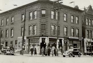 Three-storey brick building at corner of intersection, with shop windows at ground floor.