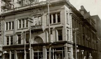 Façade of three-storey stone building visible from mid-level of ground floor up. Sign above str ...