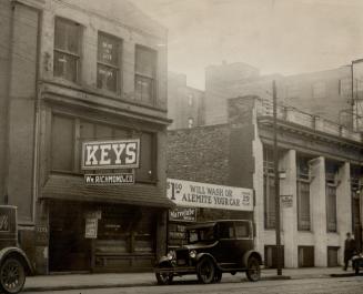 Street view of two brick building façades with sign reaching over the lot between them reading,…