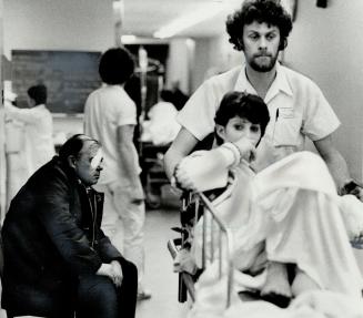 Attendant Francois Morin wheels a patient past an eye-injury victim at East Genera