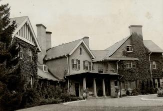 Exterior of three-storey, brick house with dark shutters and prominent chimney stacks; vines co…