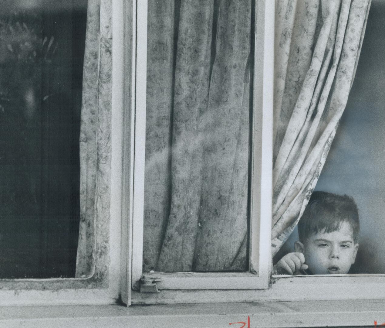 Sad-faced child stares out through broken window in one of 732 housing units in Toronto's run-down Regent Park South housing project