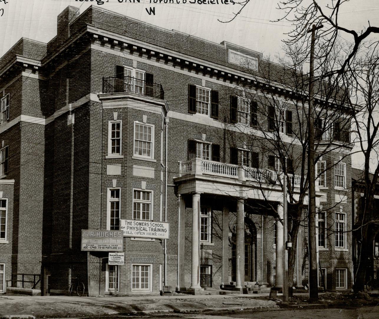 Façade of four-storey brick building with four pillars supporting a narrow, second floor porch …