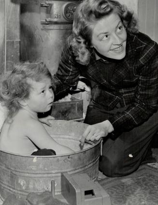 A young Islander, baby Sue Adam, whose dad's a flier, gets a bath by the stove