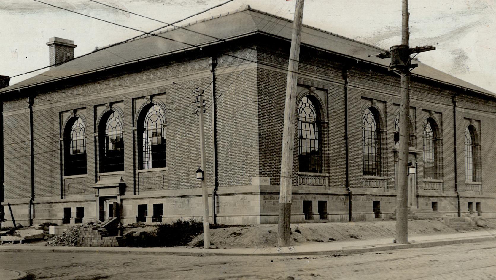 Corner view of one-storey brick building with arched windows and stone entrance steps on two si…