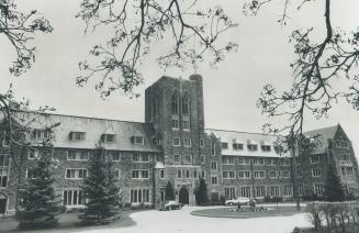 Four-storey brick building with gable roof and dormer widows; belfry tower above entrance displ…