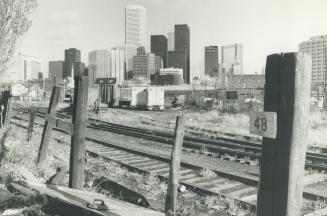 Image shows railway tracks and vacant land behind them as well as high-rise Harbour buildings i…