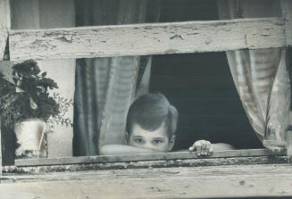 A child in Toronto's Trefan Court looks out from behind The Poverty Wall - the title of an agry new book about the Canadians living in penury