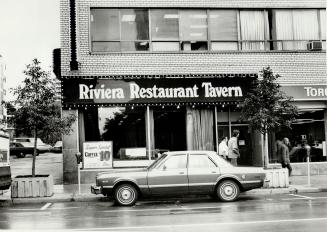 Black sign with white letters above large picture window, reads, Riviera Restaurant Tavern; sig…