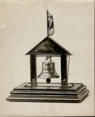 Bell suspended from slope-roofed structure mounted on beveled, rectangular base. Union Jack fla…