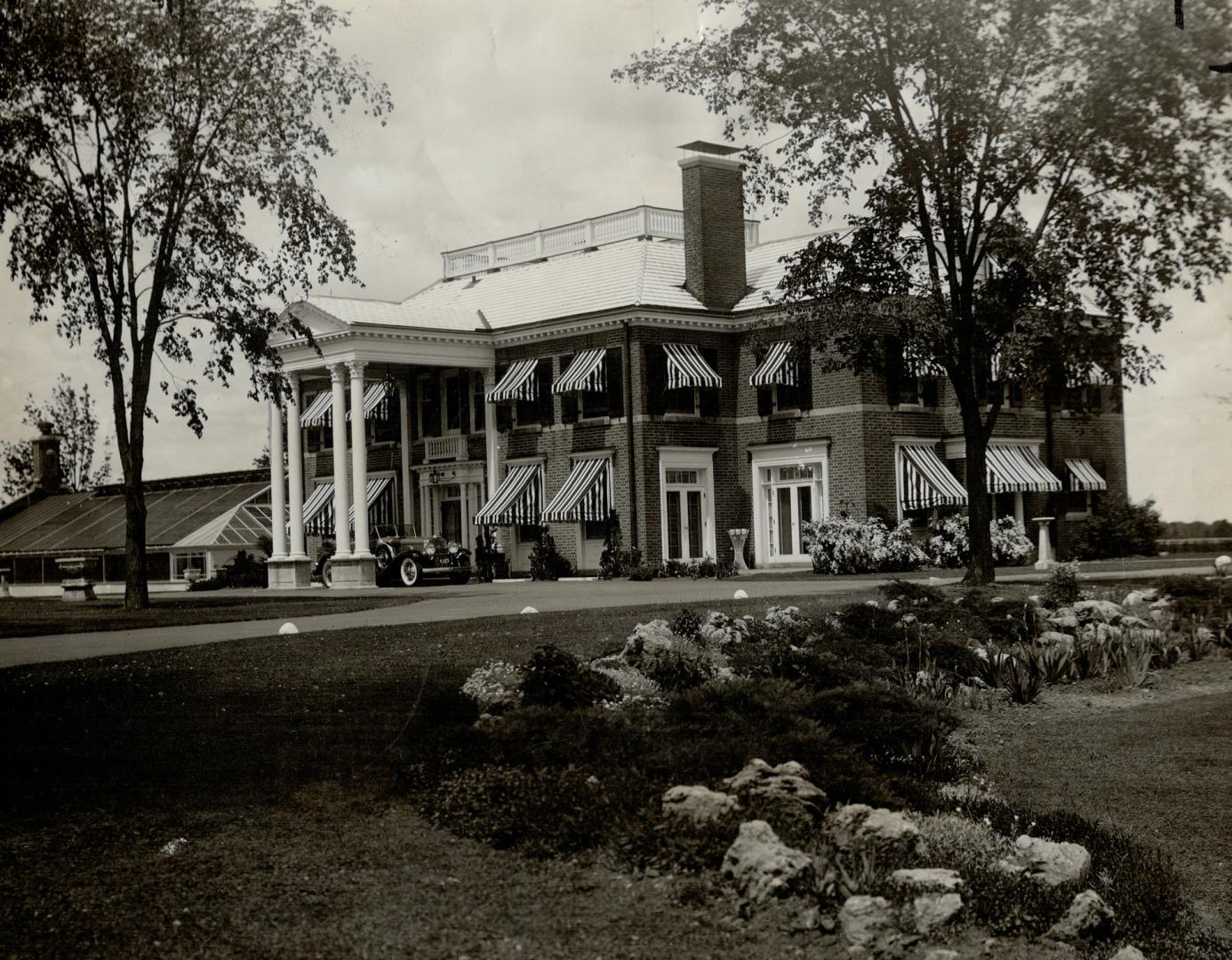 Two-storey brick house with portico at entrance. Striped, fabric awnings overhang windows.