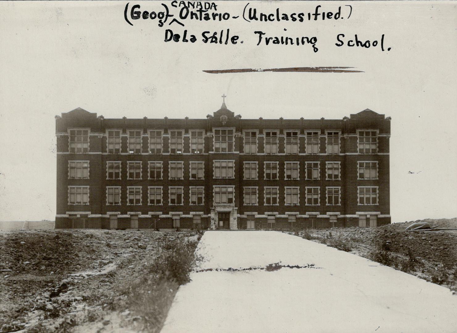 Façade of three-storey brick building with small cross standing on roof, centre.