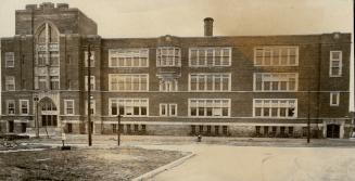 Exterior of four-storey flat-roofed brick building with double-hung windows, round chimney stac…