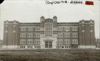 Façade of three-storey, flat roofed brick building with dark, double entrance doors.