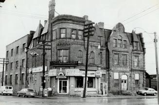 Corner view of three-storey brick building with narrow dormers. Sign above ground floor shop wi ...