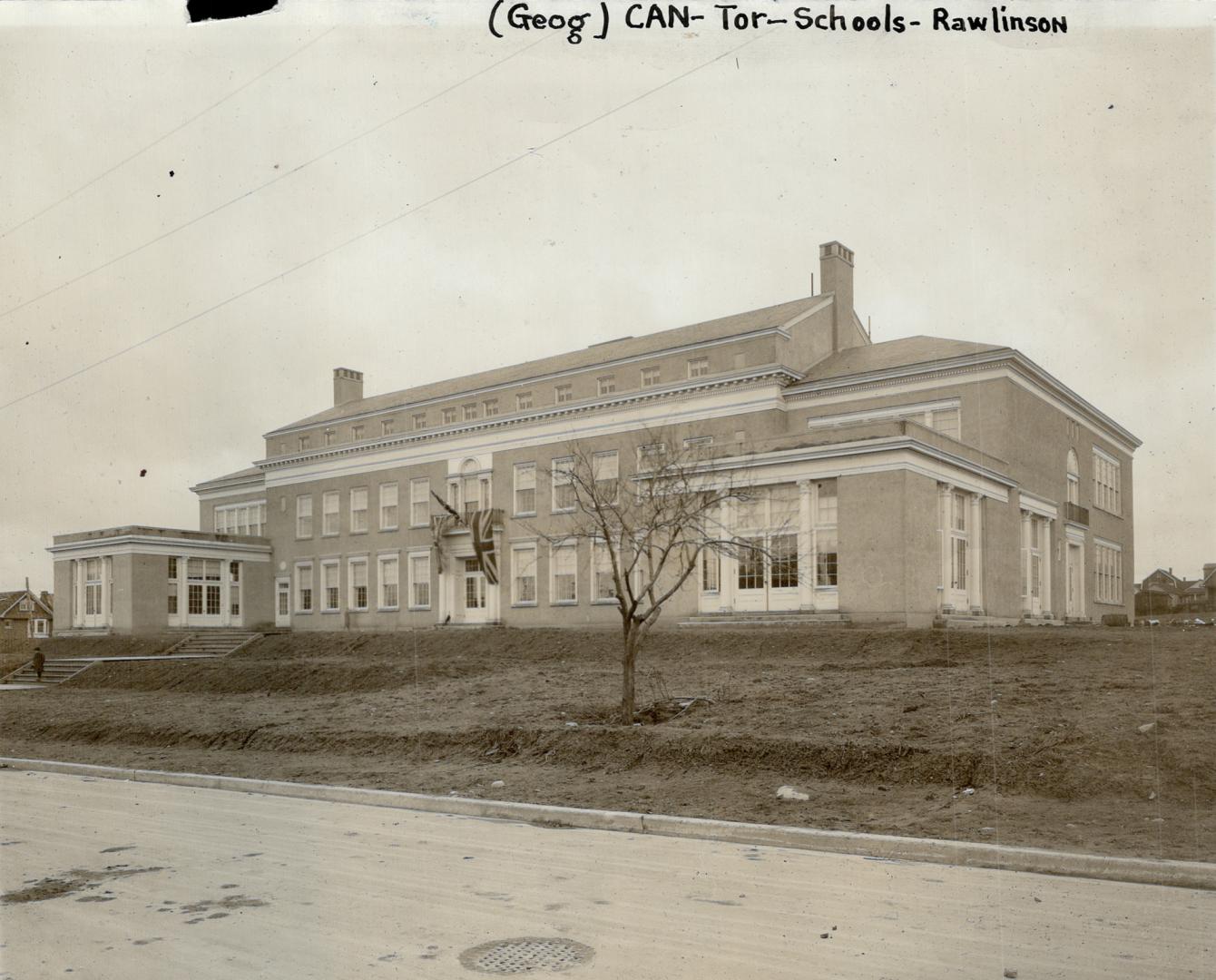 Three-storey, gable-roofed, light brick building on grassy incline. Two flat-roofed, single-sto…