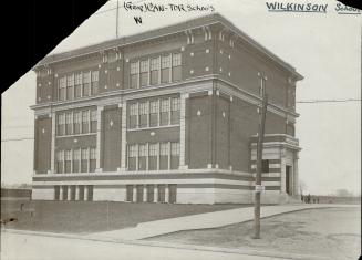 Side view of four-storey brick building with double-hung windows. A wide, paved path surrounded ...