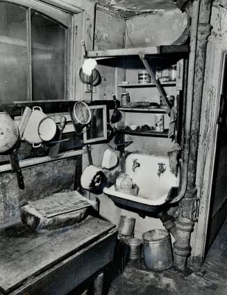 Tight view of utility sink affixed to wall above collection of empty cans and bucket on ground …