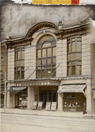 Exterior of three-storey stone building with stone arch detail over windows, centre. An awning …