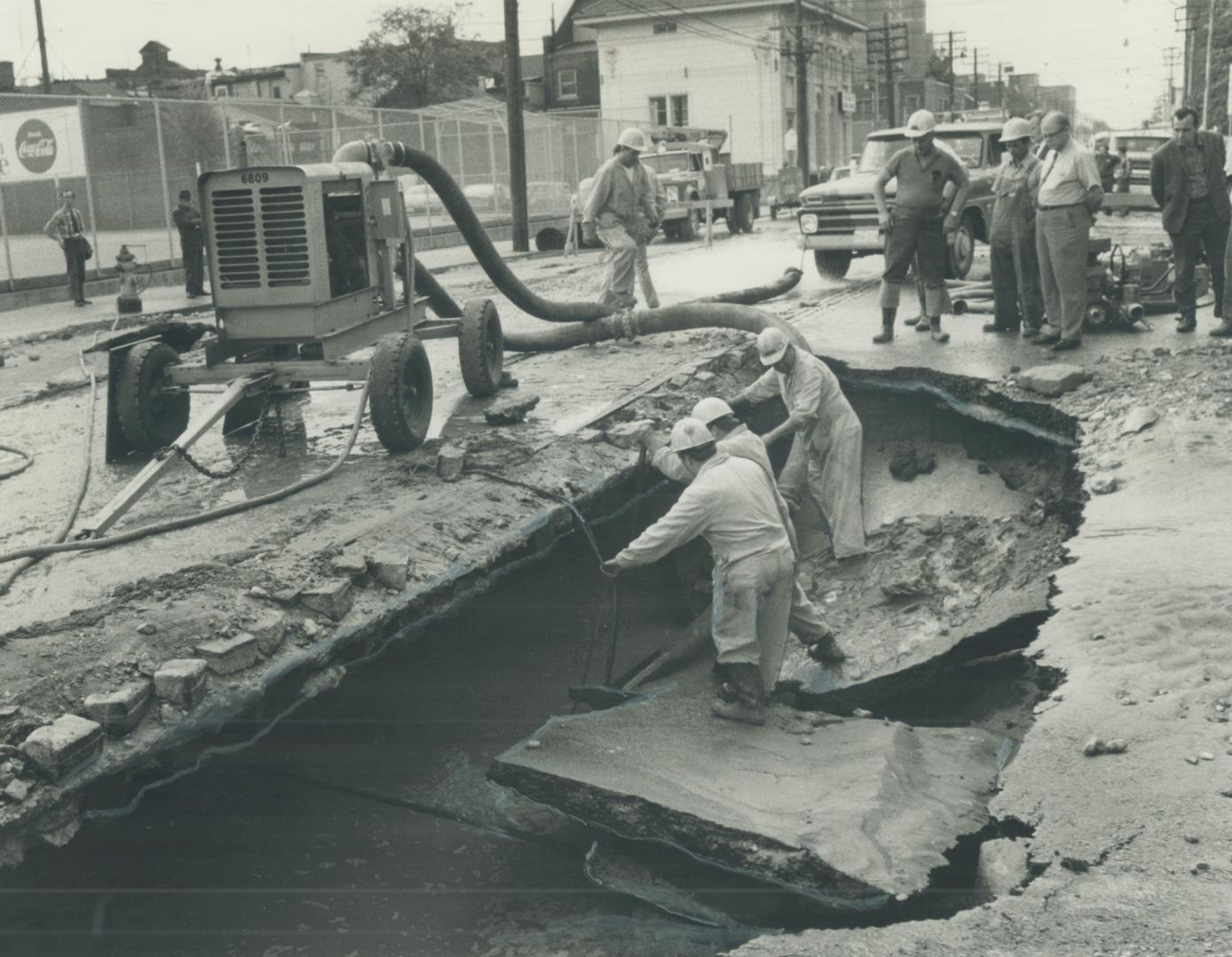 Image shows a crater in the street and some workers around it.