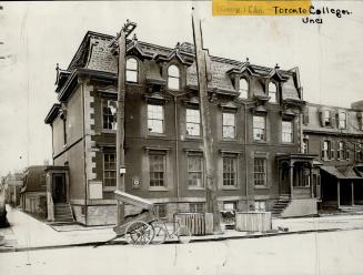 Three-storey brick structure with Mansard roof and dormer windows. Sign attached to leftmost gr…