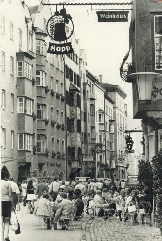 Downtown Innsbruck, in Austria: In the pedestrian mall gingerbread buildings of pastel and gilt look down on people eating peacefully